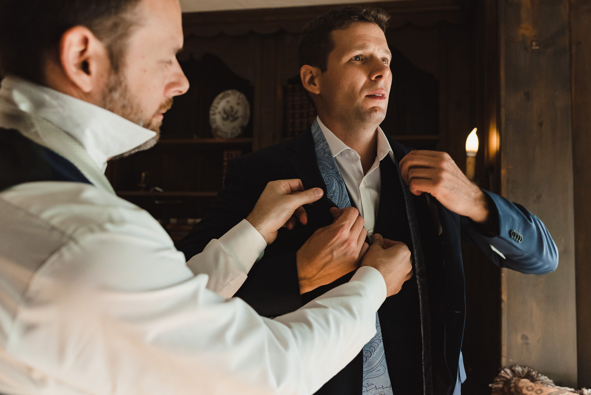 groomsman in white dress shirt helping groom put on his light blue tie over navy suit before wedding at La Paletta Mansion in Burlington Ontario