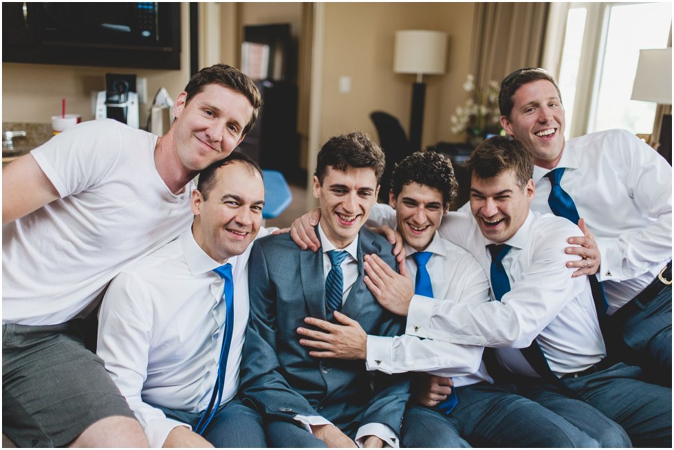 Groomsmen squished on a couch with the groom laughing and smiling