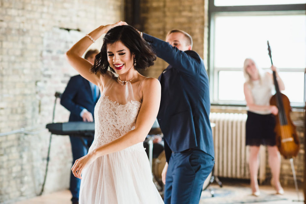 bride being twirled by her groom as they dance in front of their wedding band at the Jam Factory Toronto