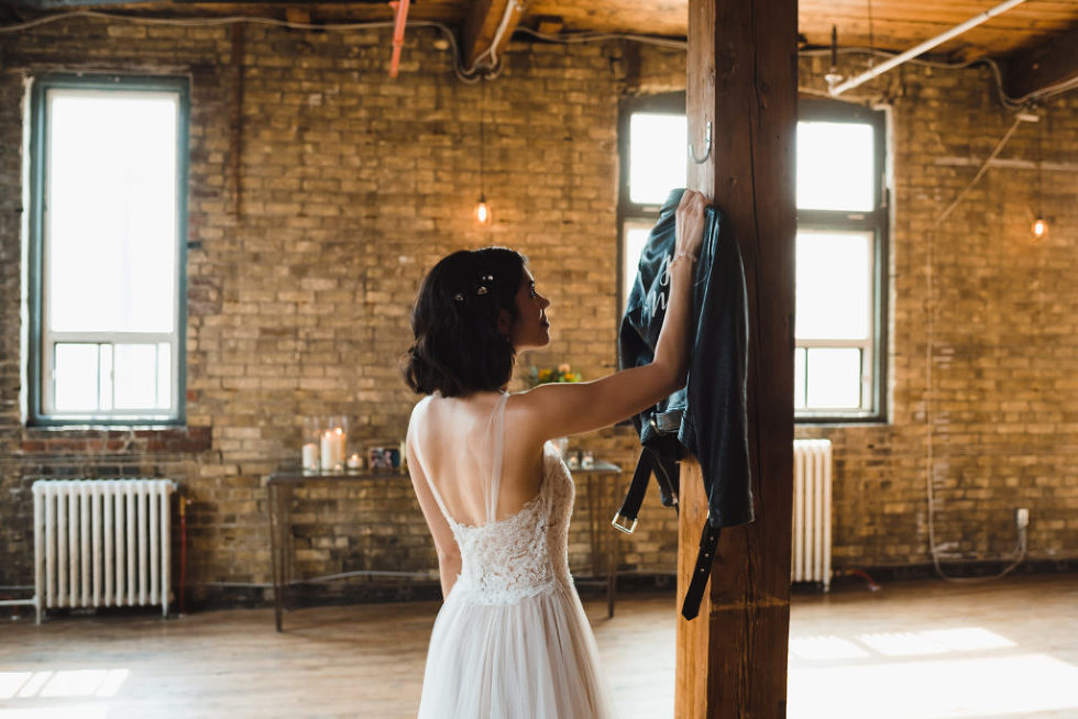 bride reaching for her just married leather jacket hanging on wooden post at the Jam Factory Toronto wedding photography