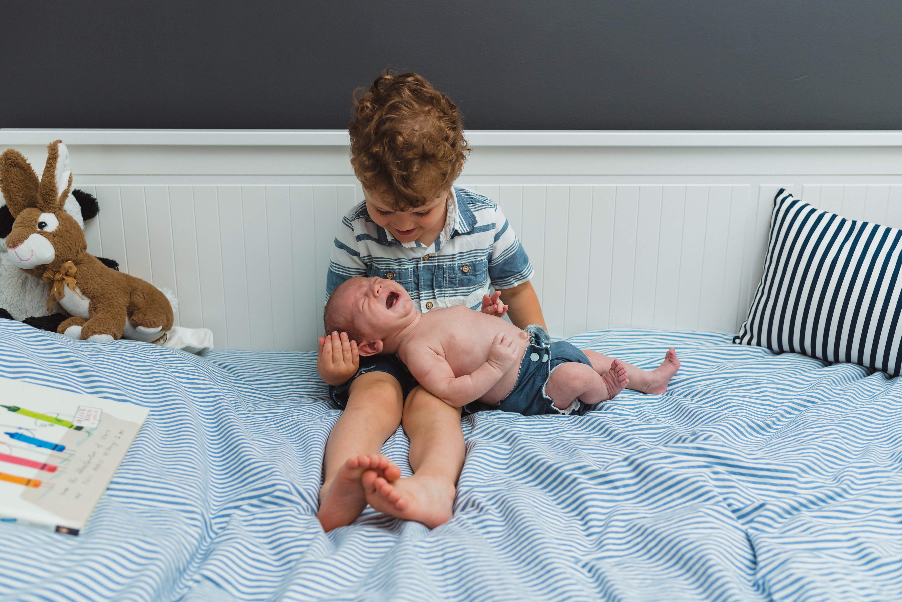 toddler sitting in his bed holding baby brother for newborn photo session