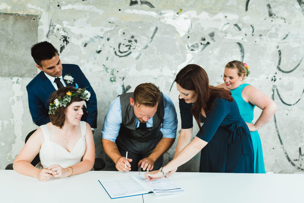 bride and groom watch as officiant shows groomsman where to sign wedding certificate Toronto Junction Craft Brewing