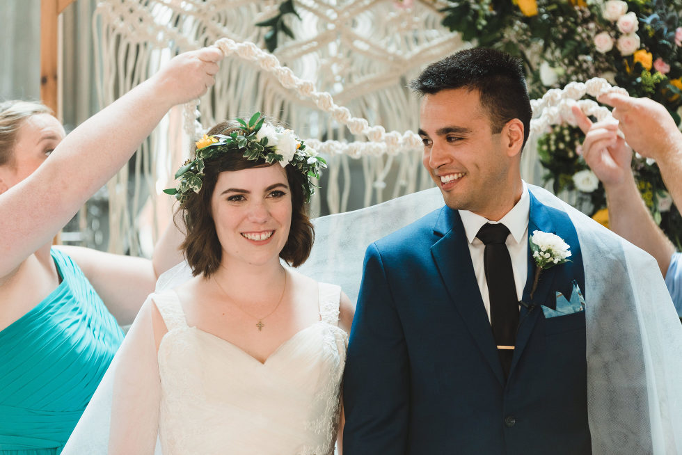 bride and groom smile as white decorations are placed upon them during ceremony Toronto Junction Craft Brewing wedding photographer Gillian Foster