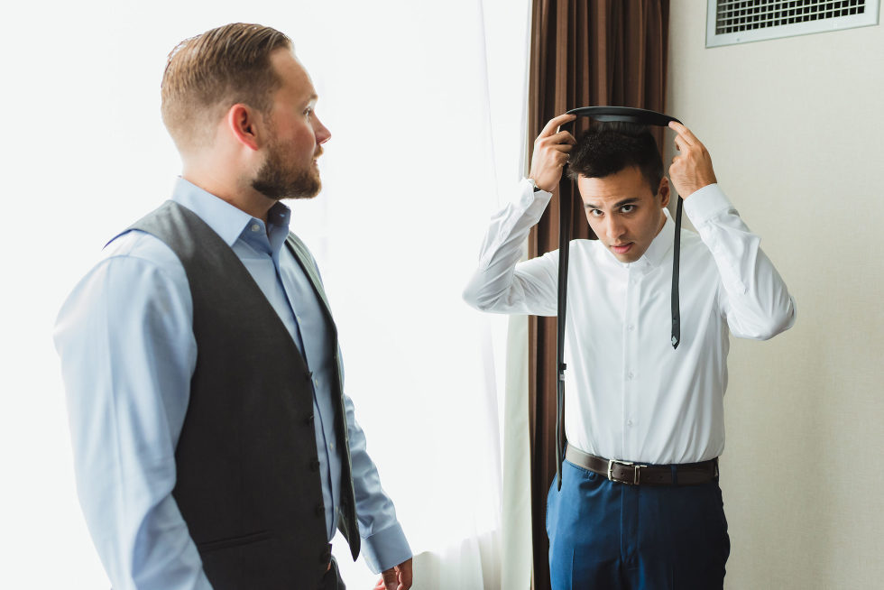 groomsman watching as groom is about to place his tie around his neck Toronto Junction Craft Brewing wedding venue