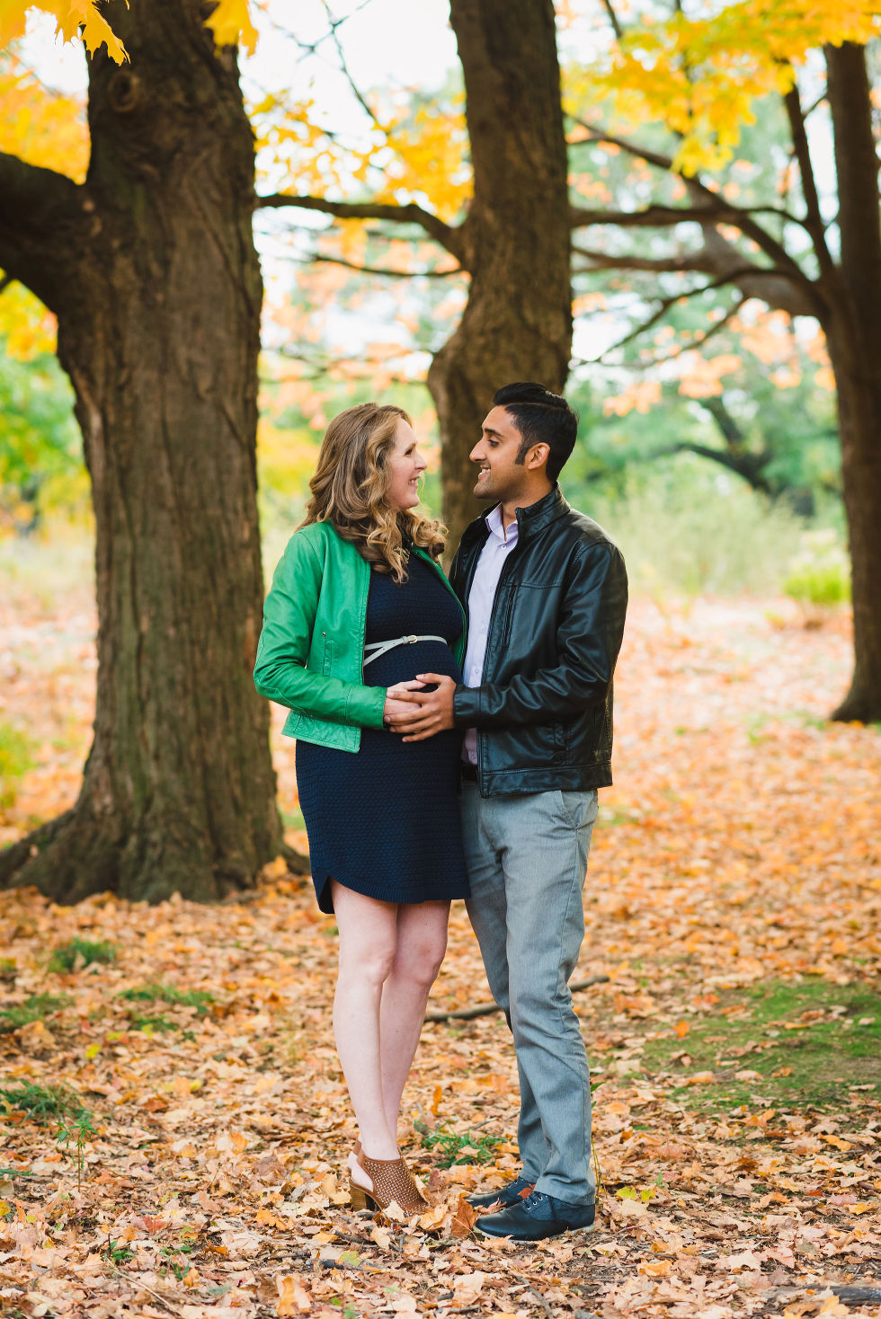 pregnant couple embracing each other under autumn leaves in High Park, Toronto