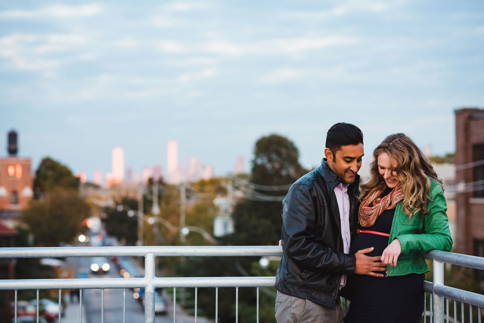 man holding his partners pregnant belly as they stand on platform with Toronto cityscape in background