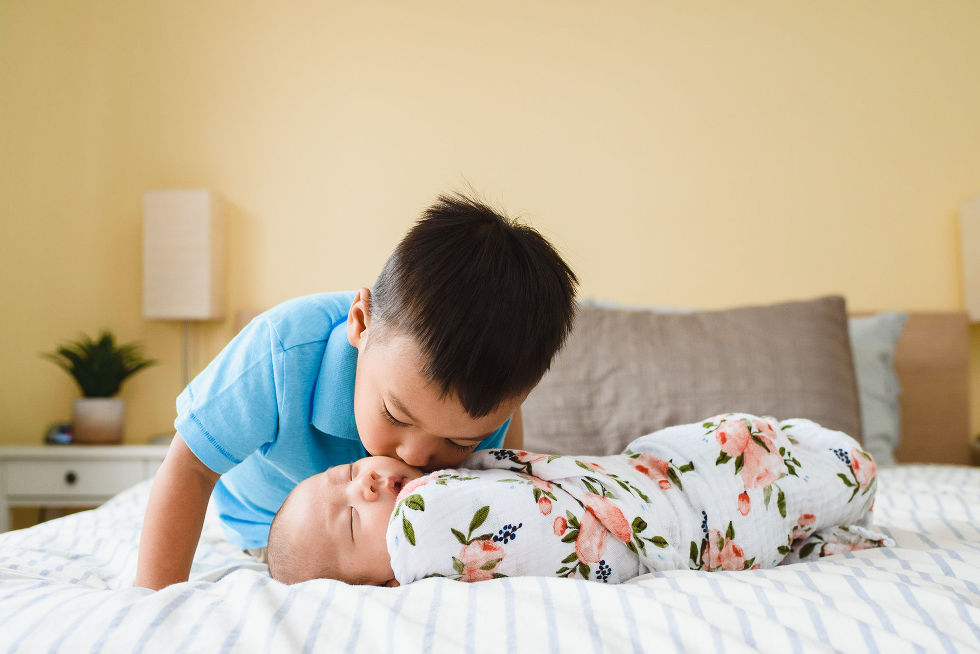 toddler crouching down to kiss his newborn sibling that