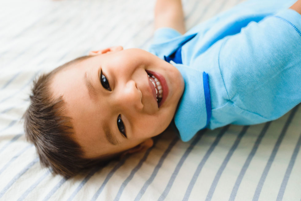 toddler smiling as he lays on parents bed during his newborn siblings